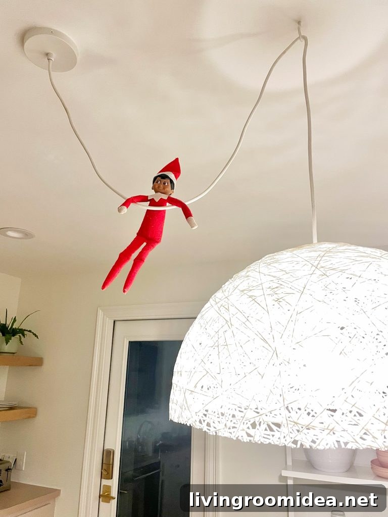 Elf on the Shelf hanging from pendant light cord in kitchen