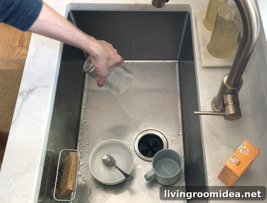 Hand removing dirty glass from dirty stainless steel sink for cleaning