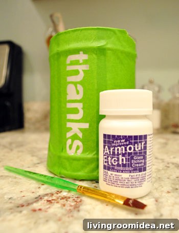 Glass etching cream and paintbrush next to glass jar with DIY tape stencil