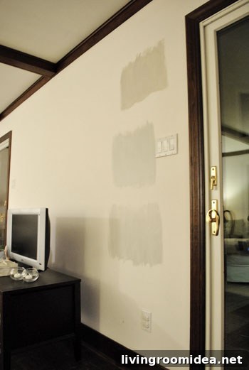 three Benjmain Moore gray paint color swatches on a white wall at night time in artificial light