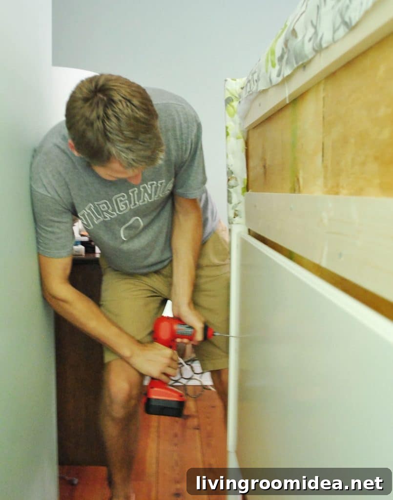 John screwing DIY upholstered headboard onto frame from backside of bed