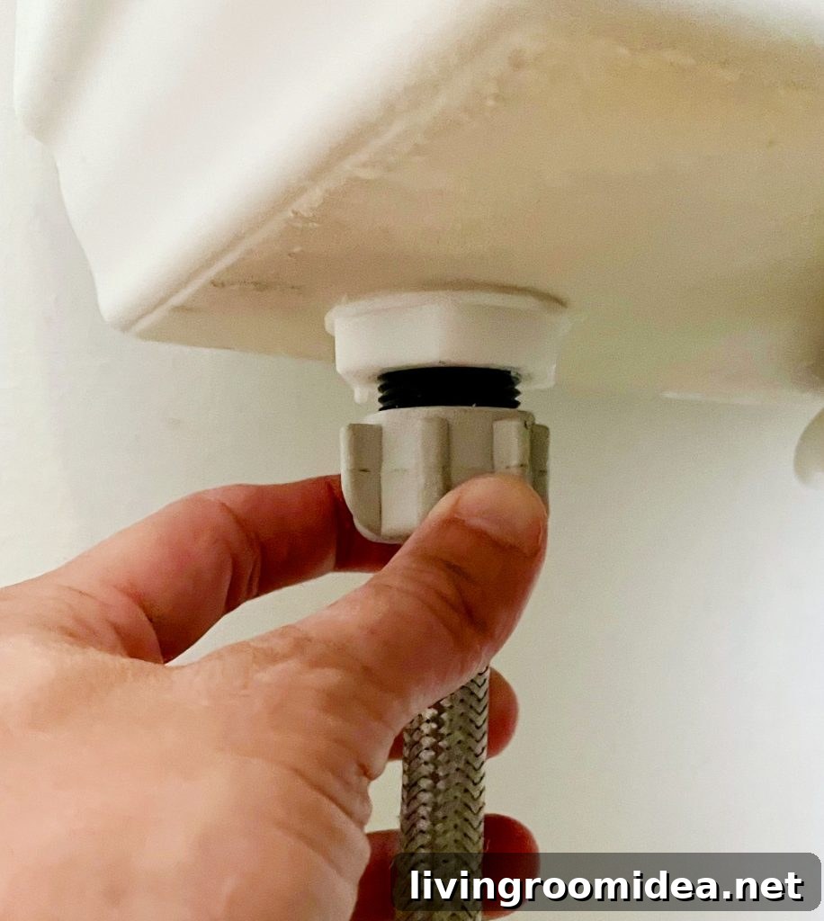 Hand Loosening Water Supply Line Under Toilet Tank